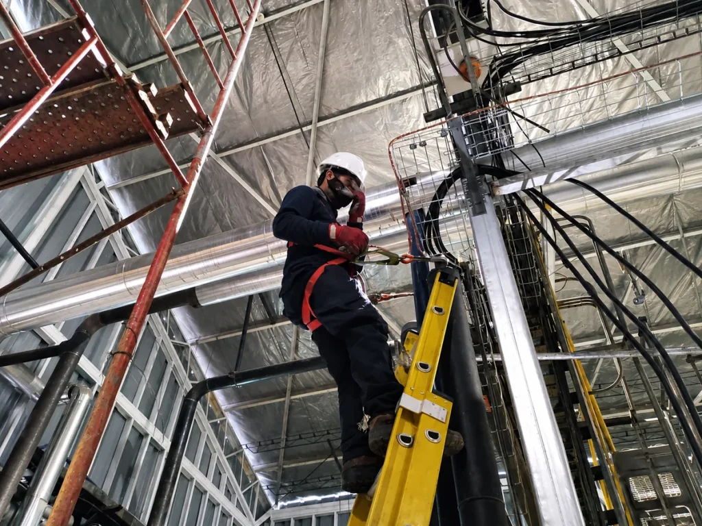 Técnico eléctrico con arnés de seguridad realizando montaje en terreno